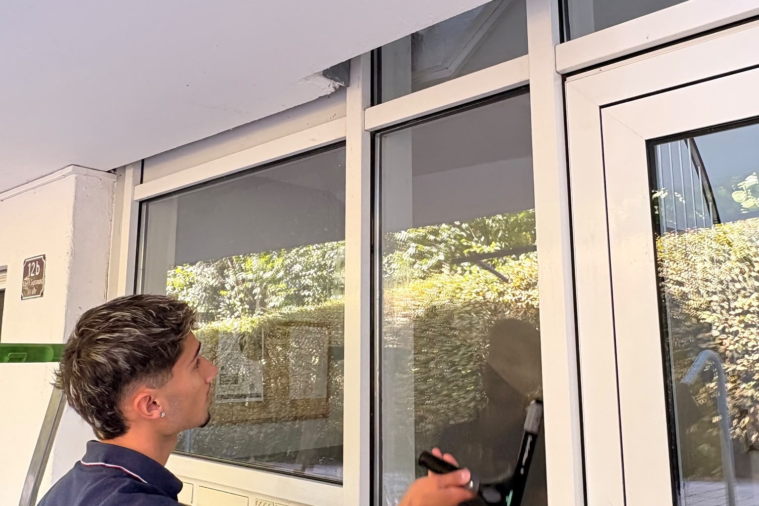Mitarbeiter reinigt mit dem Abzieher eine grosse Glasfront im Eingangsbereich